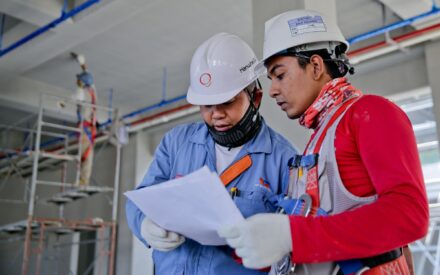 two workers in hard hats reviewing information on paper